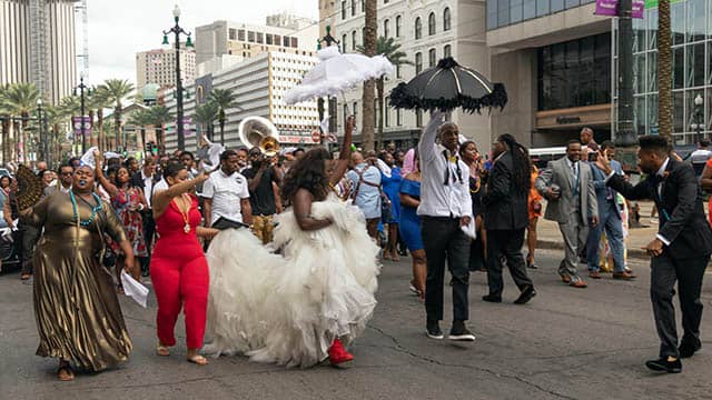 a large group of people in wedding attire parade through the streets with musicians