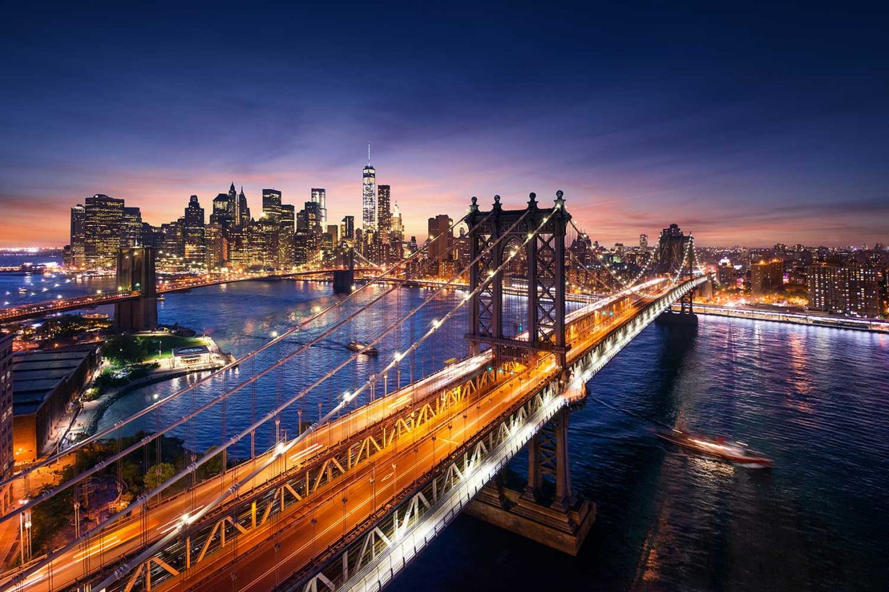 a view of the New York City skyline at night as seen from the other side of the Manhattan Bridge.