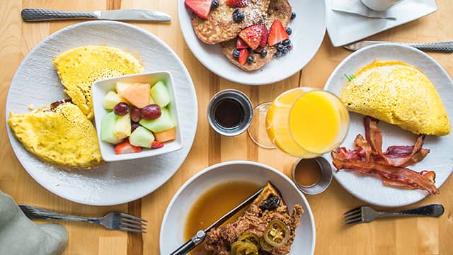 an overhead view of a table with omelets, pancakes, chicken and waffles, and a mimosa