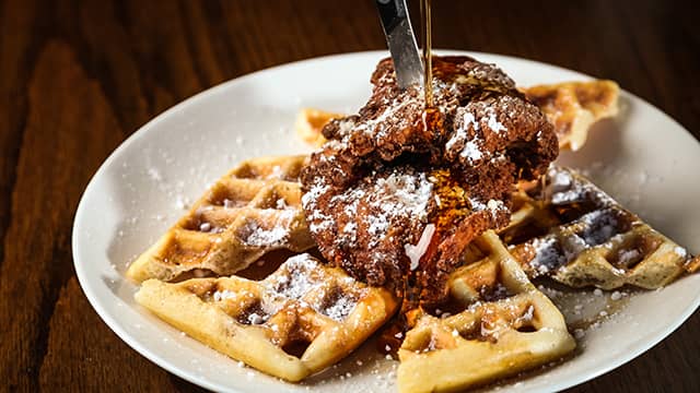fried chicken on waffles topped with powdered sugar and maple syrup