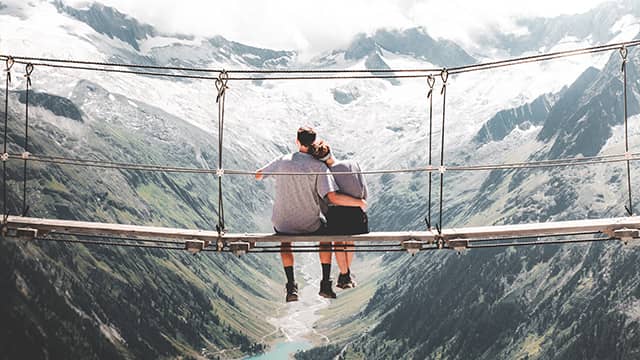 two people sit next to each other on a bridge suspended over a canyon