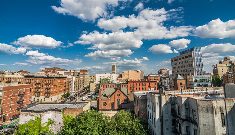 an aerial view of Harlem in New York City with a blue sky and fluffy white clouds in the background