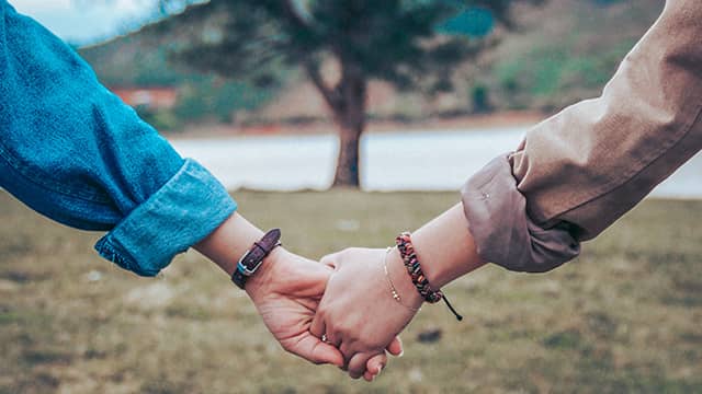 two arms holding hands in front of a tree