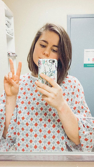 a young woman in a hospital gown taking a photo of herself in the mirror