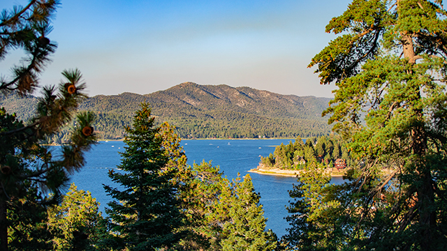 green pine trees frame a blue lake with mountains in the background