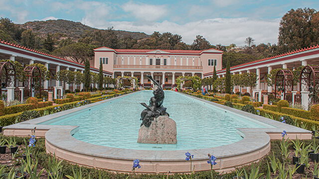 a view out over a pool with a statue in the middle and a large pink villa behind it