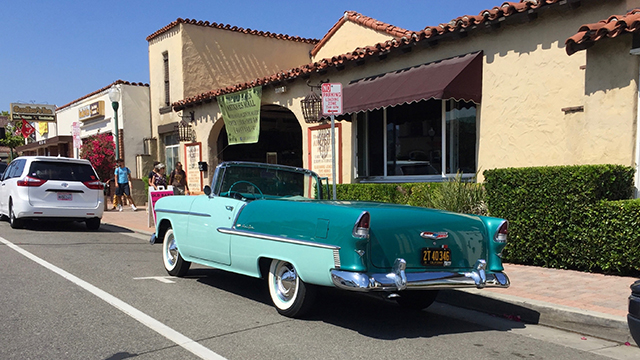 a blue classic car parked on the street in front of mission-style buildings in san juan capistrano