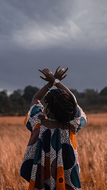 a woman stands in a field with her back to the camera and her hands in the air