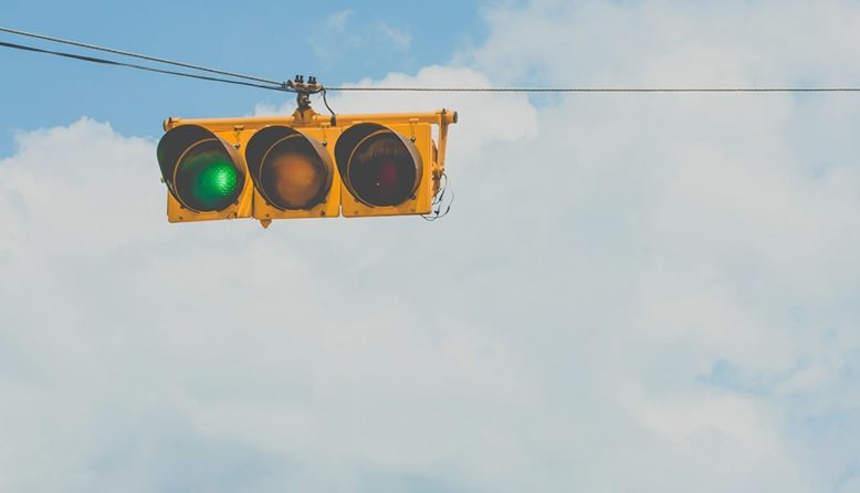 a horizontal traffic light with the green illuminated against a background of clouds