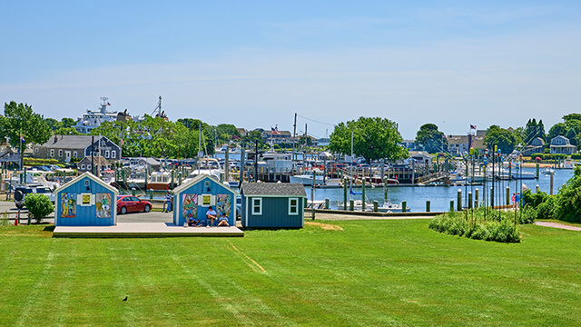 a large green lawn with colorful artist's shanties along the harbor in Hyannis, MA