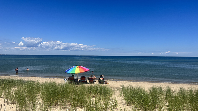 a group of people with a rainbow umbrella sit on the sand at Joseph Silvia beach on Martha's vineyard