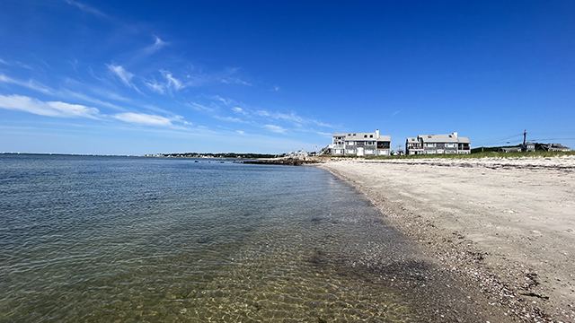 clear water and white sand at Kalmus beach in Hyannis with large beach houses in the distance