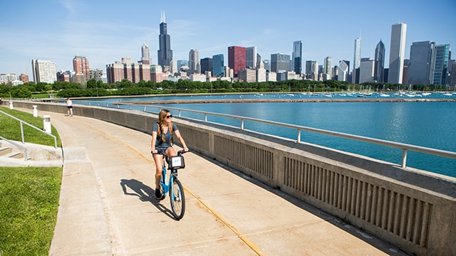 a woman rides her bicycle along the lakefront with the chicago skyline in the background