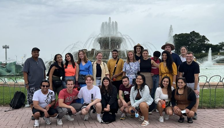a large group of young people from all over the world stand in front of a large outdoor fountain