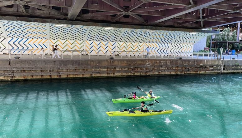two colorful kayaks paddle through turquoise water below a bridge