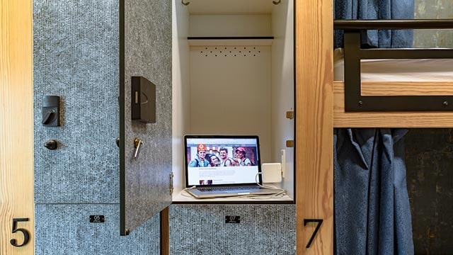 a laptop charges inside of a locker next to bunk beds in a modern hostel dorm room