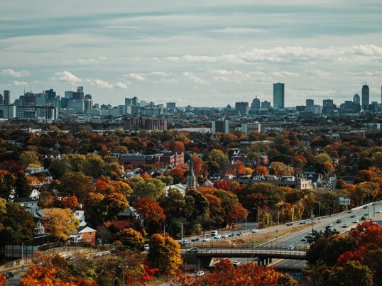 the skyline of Boston behind trees with red and yellow leaves