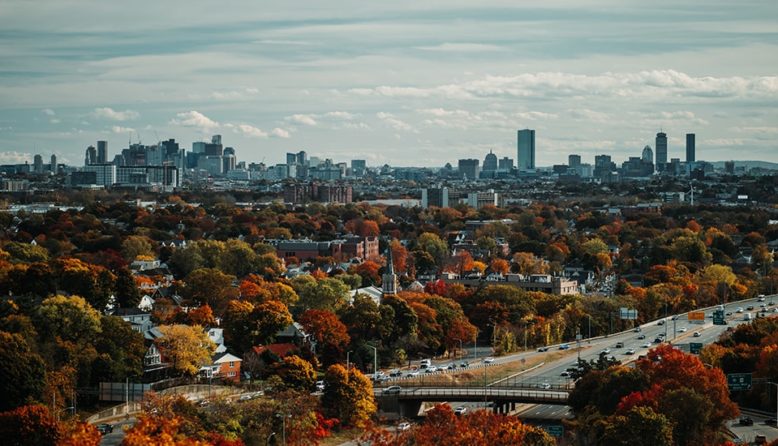 the skyline of Boston behind trees with red and yellow leaves