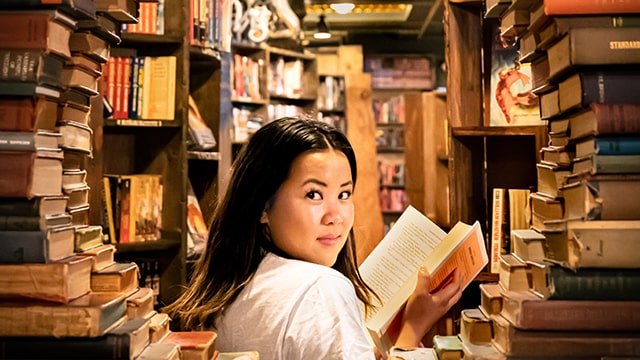 a woman holding an open book is seen through a round frame made of books