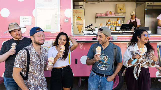 a diverse group of young people eat ice cream in front of a pink truck