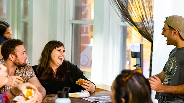 a group of young people standing and sitting around a large table laughing