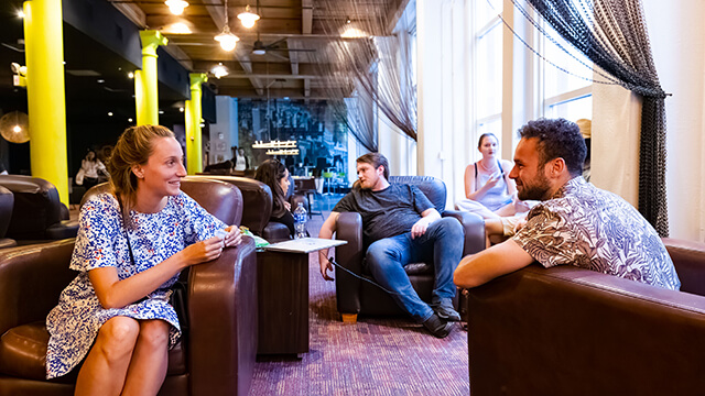 young people sit in brown chairs talking with one another in a hostel lounge