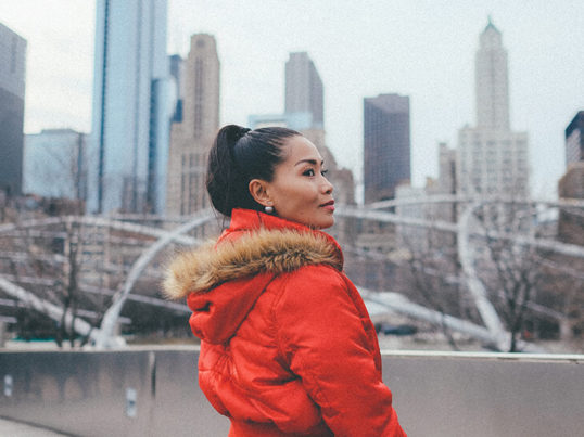 a woman in a bright red heavy coat stands in front of the chicago skyline