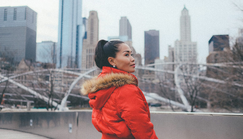 a woman in a bright red heavy coat stands in front of the chicago skyline