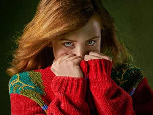 a woman hides her face behind the collar of a red sweater