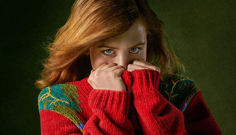 a woman hides her face behind the collar of a red sweater