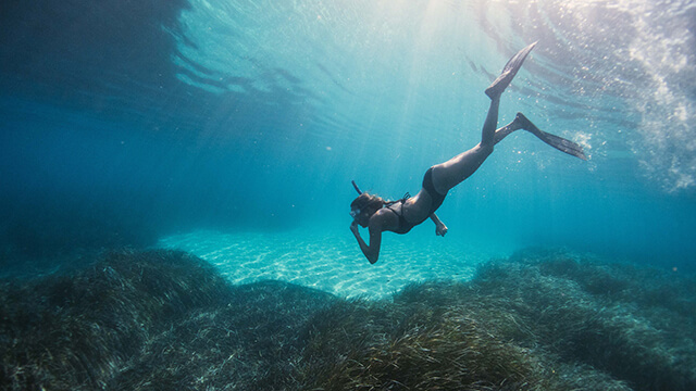 a woman snorkeling deep under clear blue water