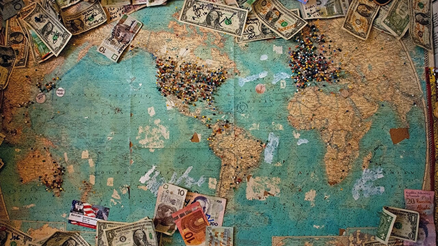 a variety of global currency on a map of the world with pins in different places