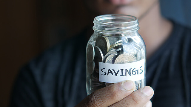 a person holds a glass jar of coins labeled "savings"