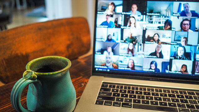 a laptop displaying faces in a zoom meeting with a mug sitting next to it on the table