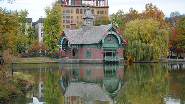 a small boathouse reflected in a pond with trees in the background