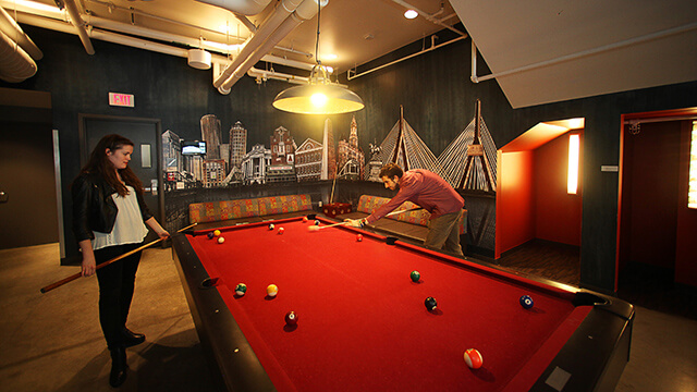 two people play pool at a red billiards table
