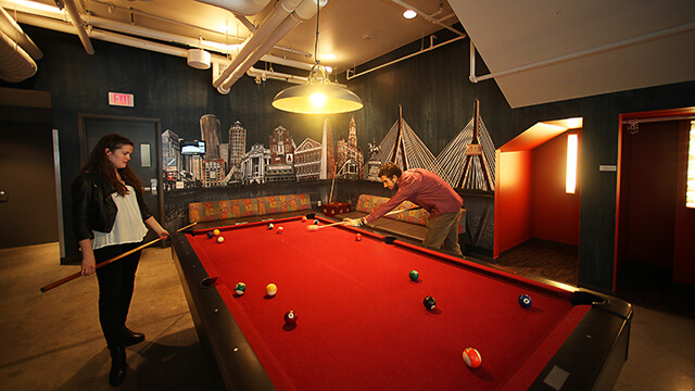 two people play pool at a red billiards table