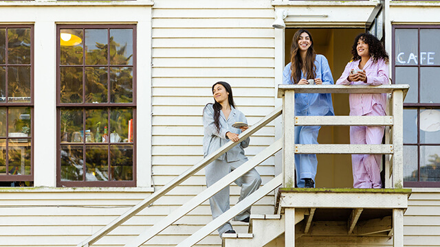 Three young female travelers stand on a staircase on the outside of a white building. They are each dressed in striped pajamas.