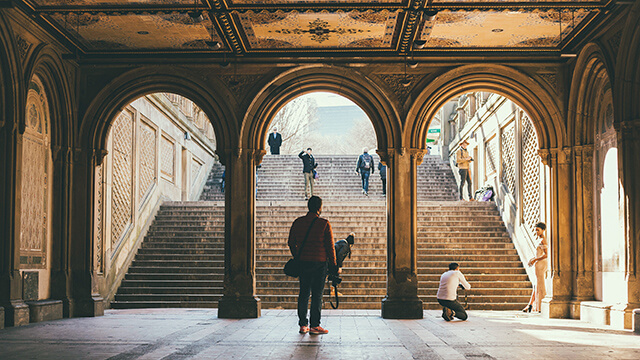 several people underneath a decorative stone archway with stairs leading out of it