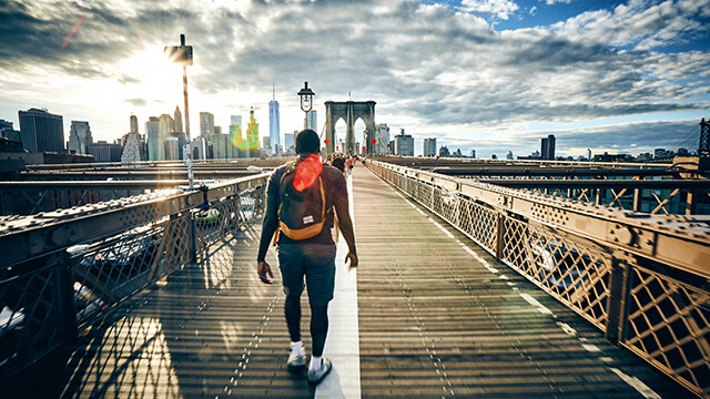 a man wearing shorts and a backpack walks across the brooklyn bridge