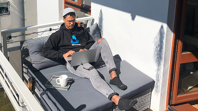 a young man relaxes outside in the sunshine while working on a laptop