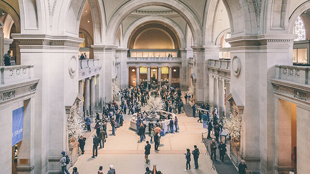people walk around the grand entryway of a museum with vaulted ceilings
