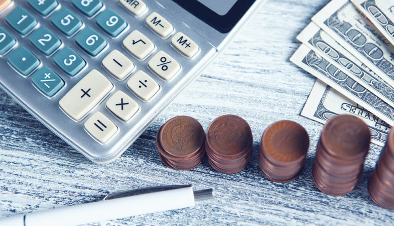 a calculator, pen, stacks of coins, and several hundred dollar bills arranged on a table ready for a traveler to make their budget