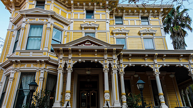 the exterior of a historic yellow and white Victorian mansion that now houses HI Sacramento hostel