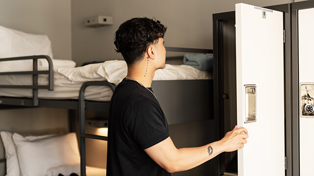 a hostel guest holds open a secure locker inside a dorm room
