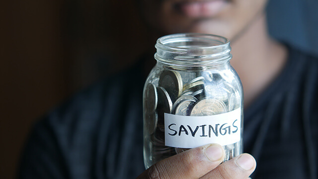 a hand holding a jar of coins labeled "savings" 