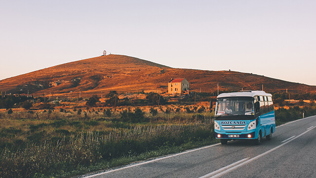 a small bus drives along a road with hills in the background