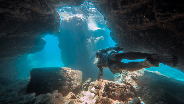 a man in scuba gear swims through a cave opening under water