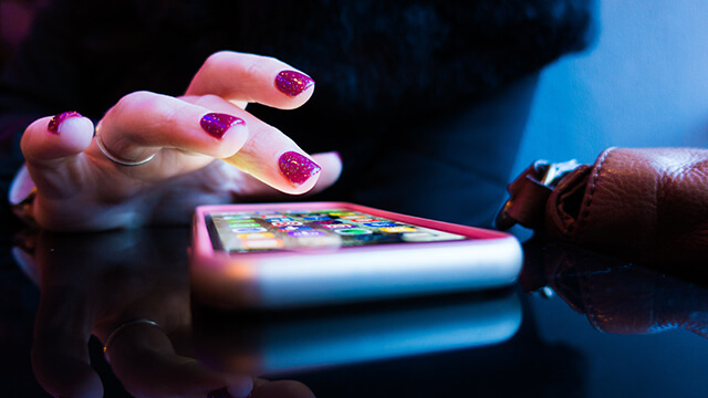 a hand with painted red fingernails taps an iphone on a tabletop