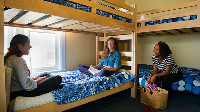 three women sit talking on on freshly made bunk beds at a HI USA hostel 